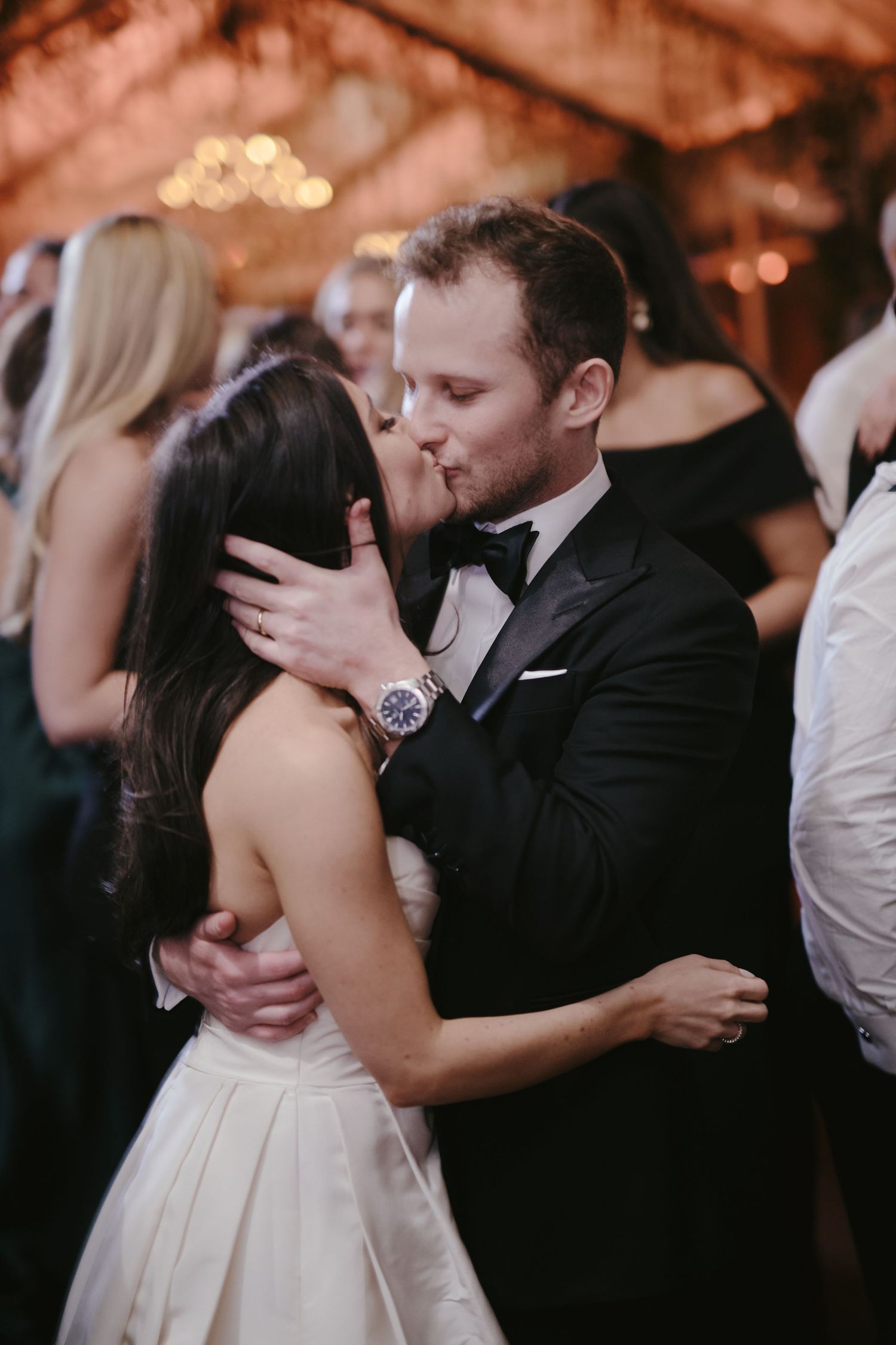 Couple shares romantic dance at elegant wedding reception with soft lighting and blurred guests in background.