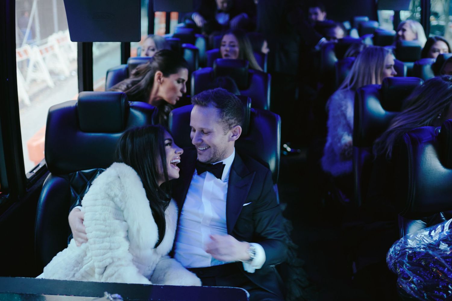 A couple shares a joyful moment while seated together at a formal event in formal evening attire.