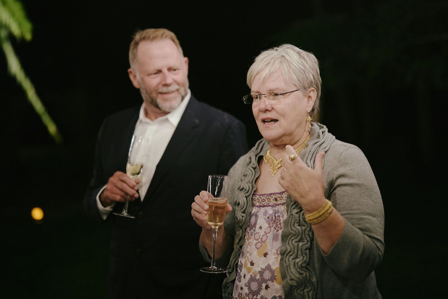Two people in formal attire holding champagne glasses share a candid moment during an evening celebration.