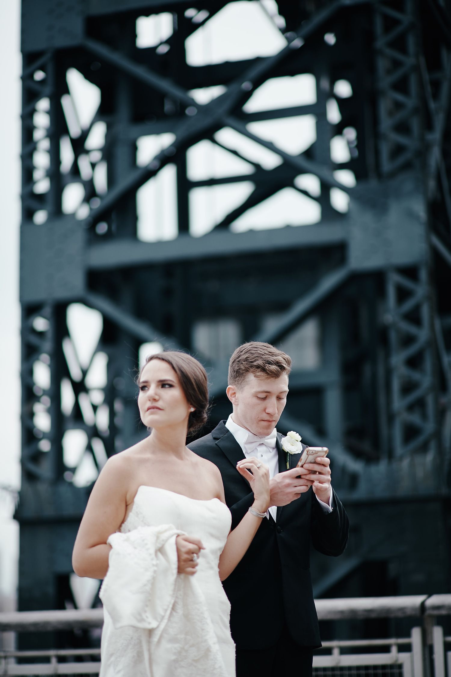 A bride and groom share ice cream cones while standing by an industrial steel bridge structure.