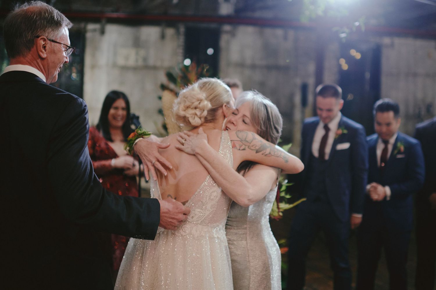 People embrace in a tender moment during an evening wedding ceremony as onlookers watch in formal attire.