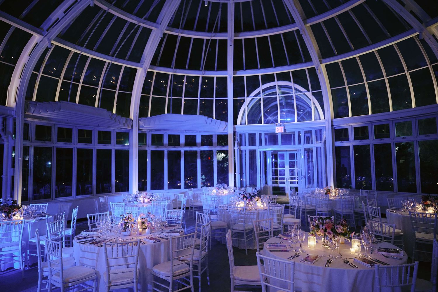 Elegant reception tables set under a dramatic glass dome lit in purple and blue lighting.