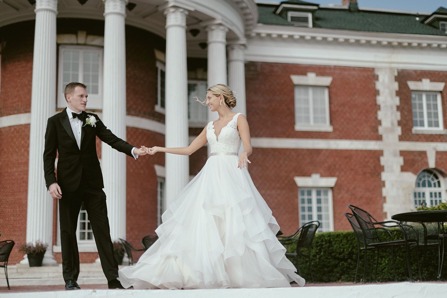 Wedding couple shares a romantic moment on steps of elegant brick mansion with white columns.