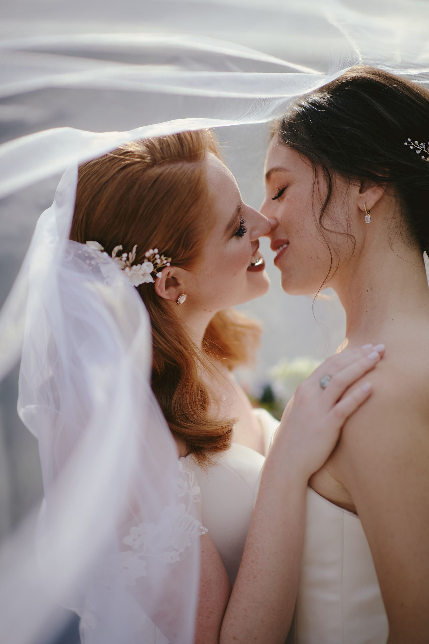 Two brides share an intimate moment under a flowing veil during their romantic wedding ceremony.