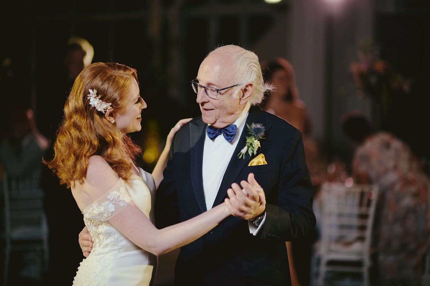Two people dance together at an elegant event, with one person wearing a white dress and the other in a black tuxedo and bow tie.
