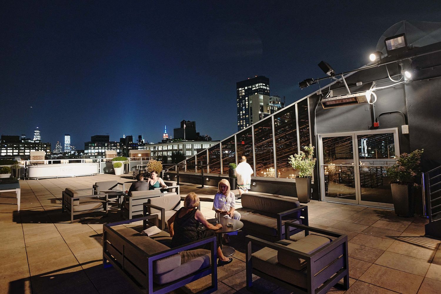 People enjoying drinks and conversation on a stylish rooftop lounge with city lights in the background at night.