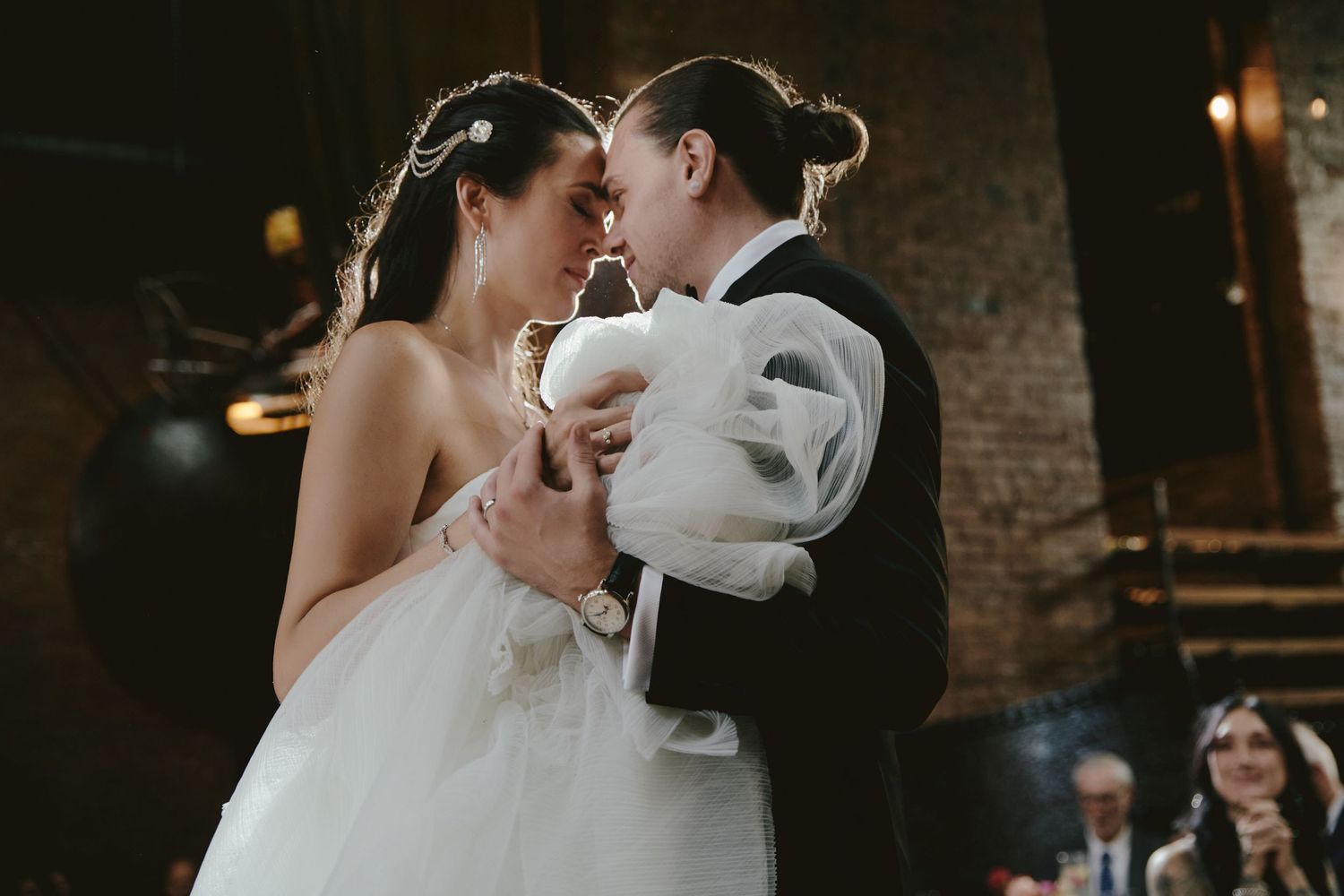 Newlyweds share an intimate dance together in a rustic brick-walled venue during their wedding reception.