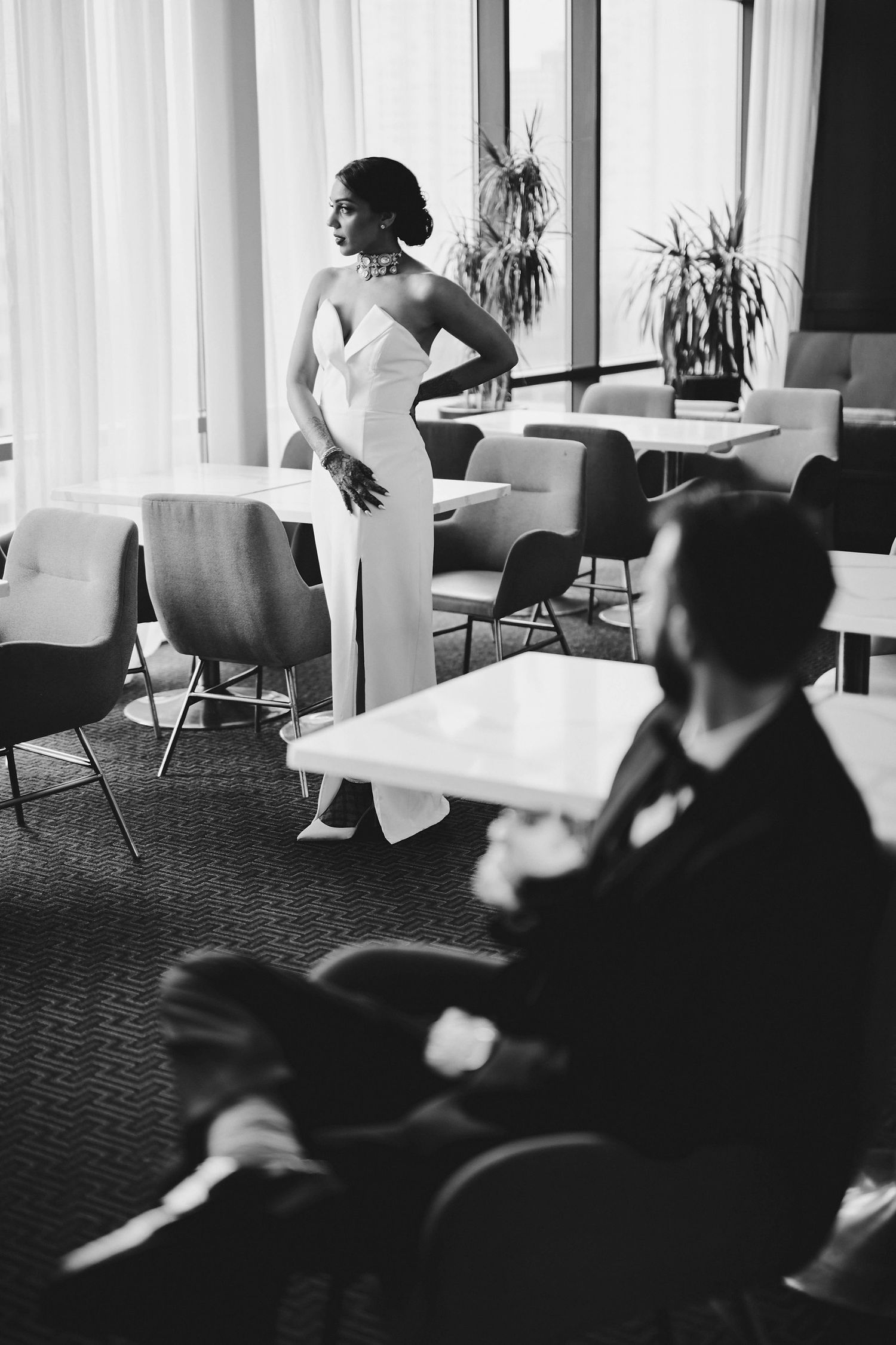 A black and white vintage photograph of a performer in an elegant white gown standing near dining tables in an empty room.