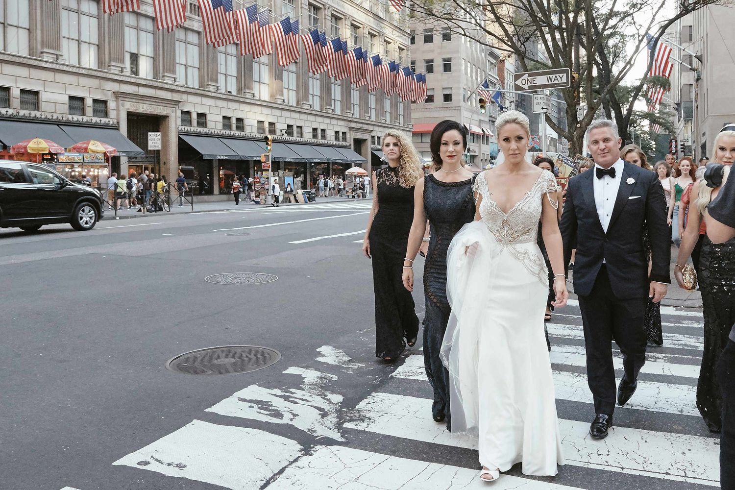 A wedding party crossing a city street in front of Macy's department store with American flags flying above.
