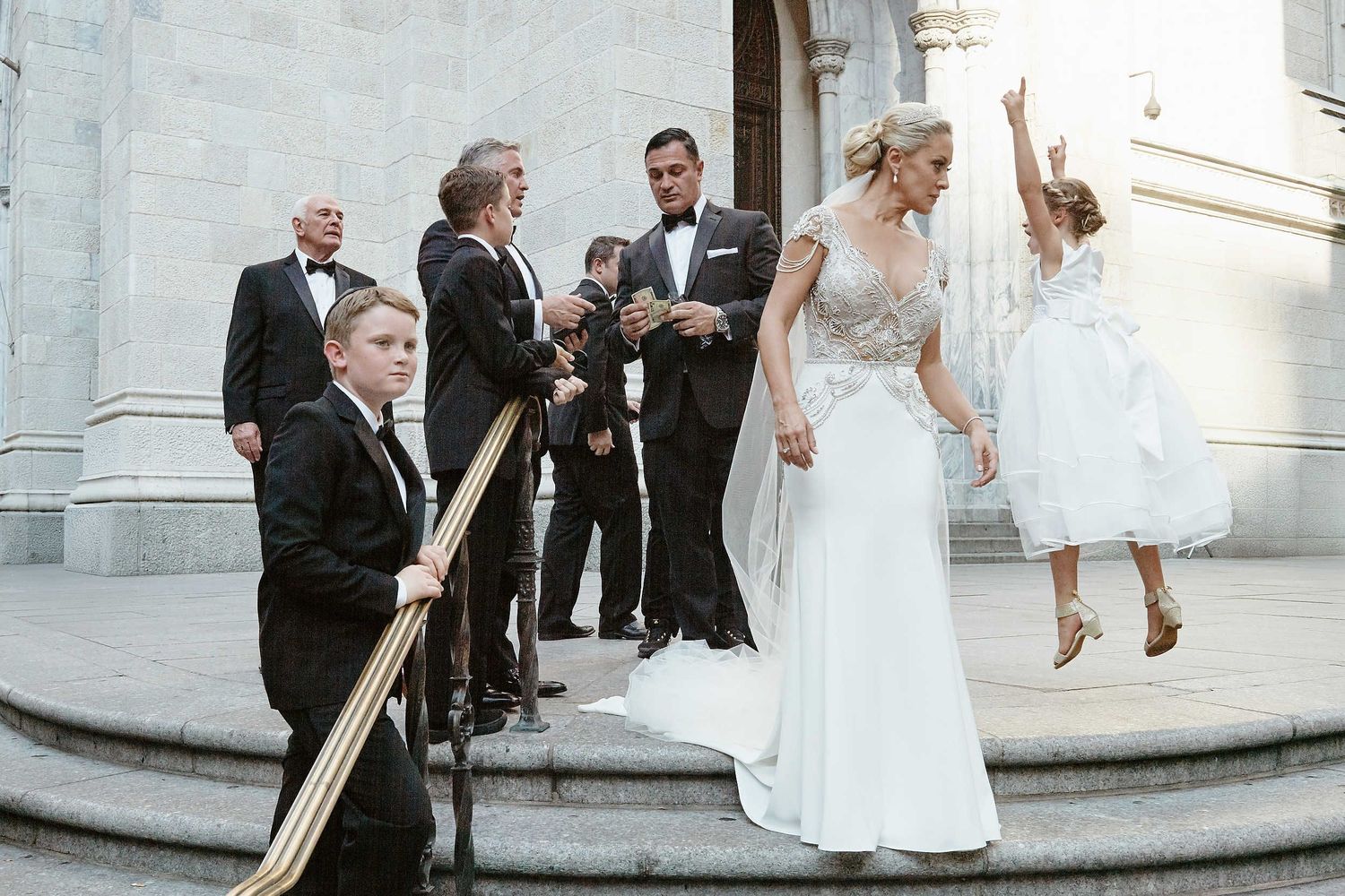 Joyful wedding party gathered on grand stone steps outside a building in formal attire.