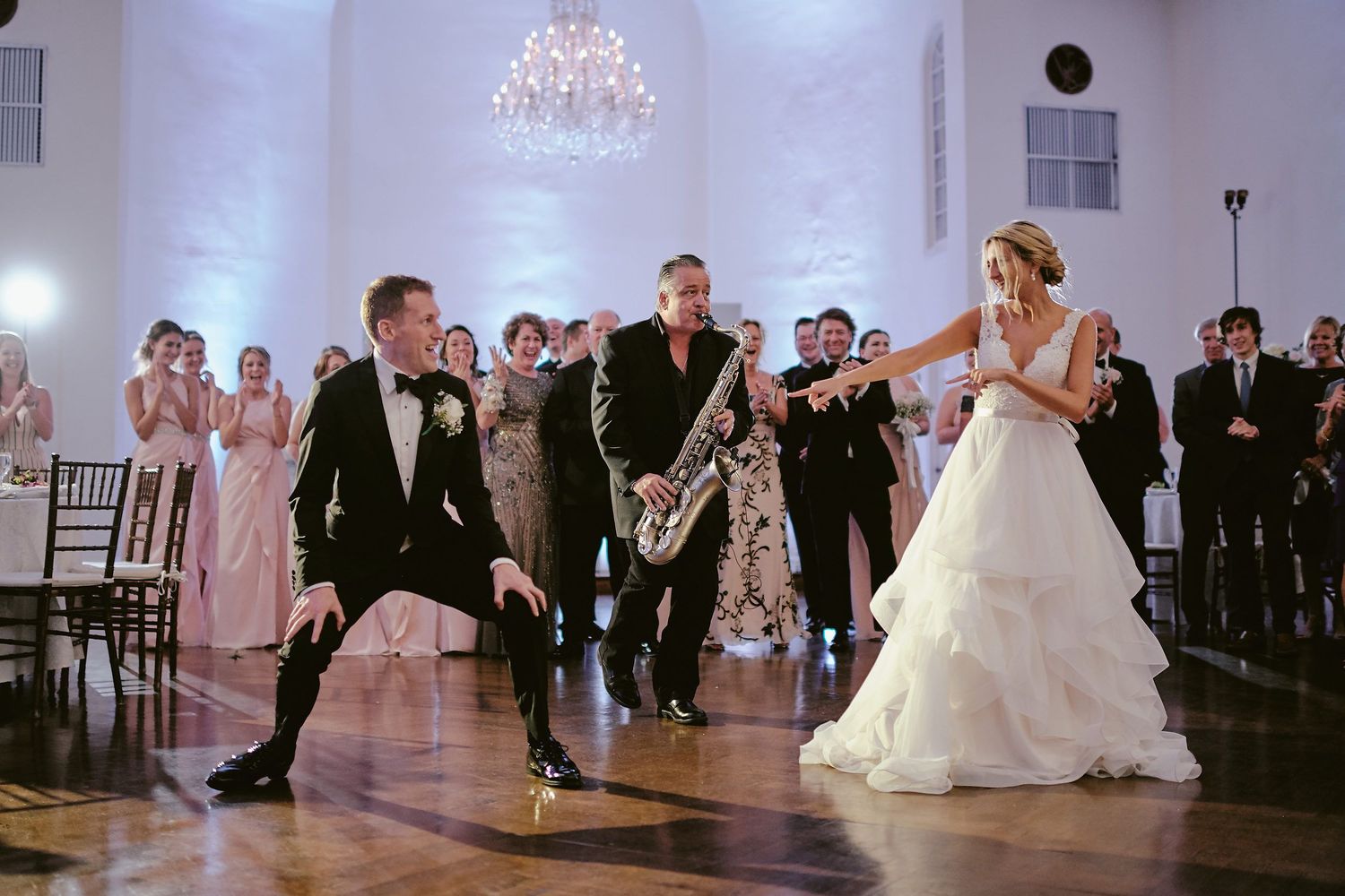 Wedding reception performers dancing with live saxophone music on polished wooden dance floor at elegant ballroom venue.