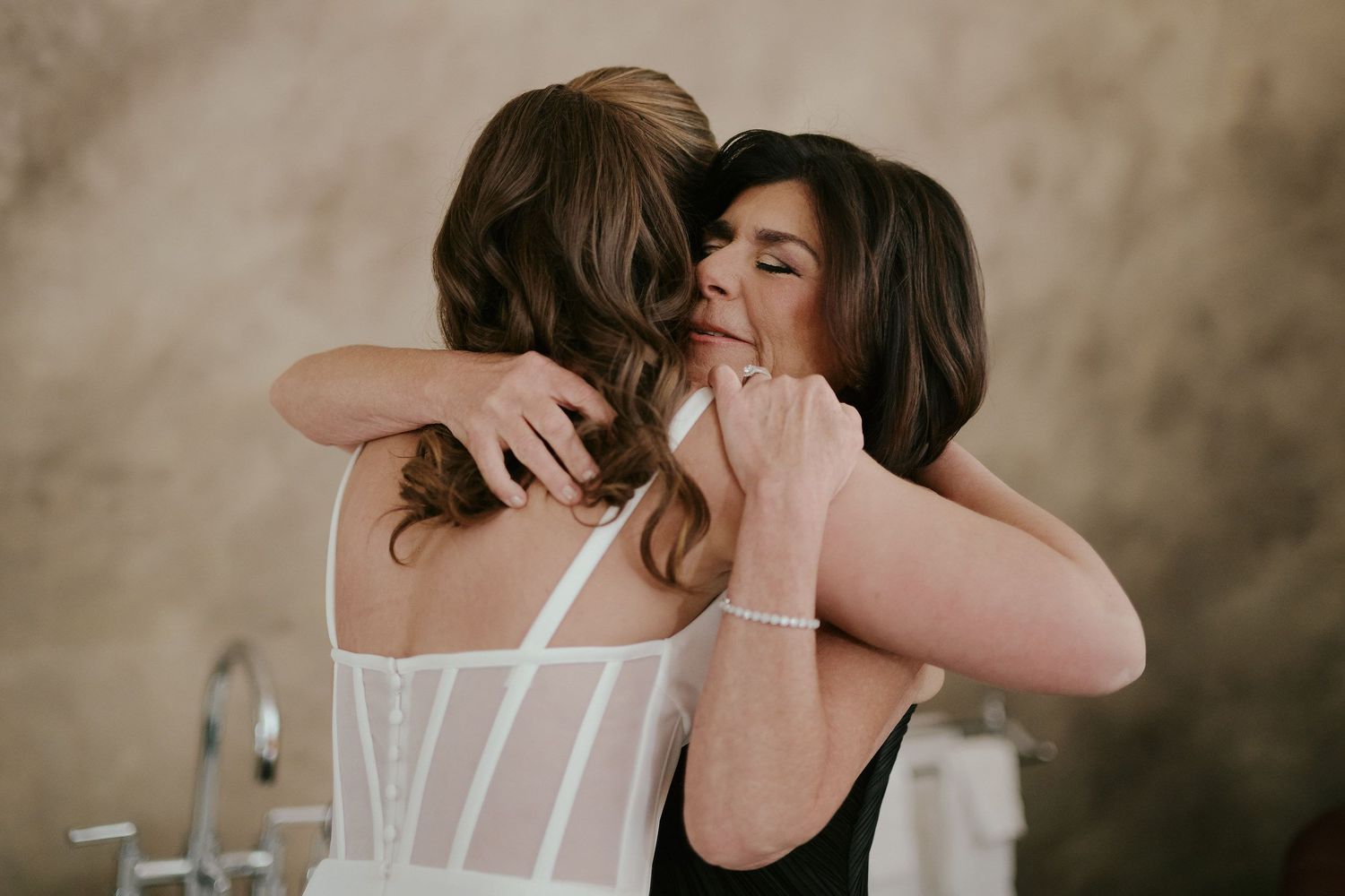Two women in wedding attire sharing an emotional embrace during a special moment.