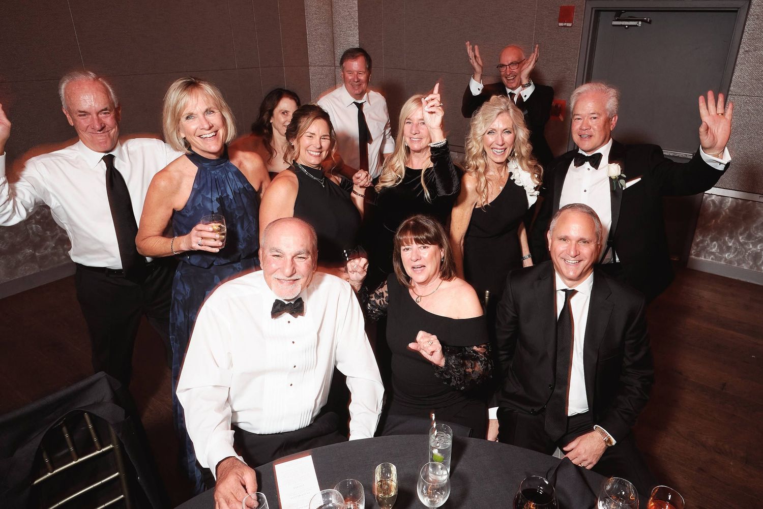 A group of formally dressed people in black and white attire pose together at an elegant evening event.
