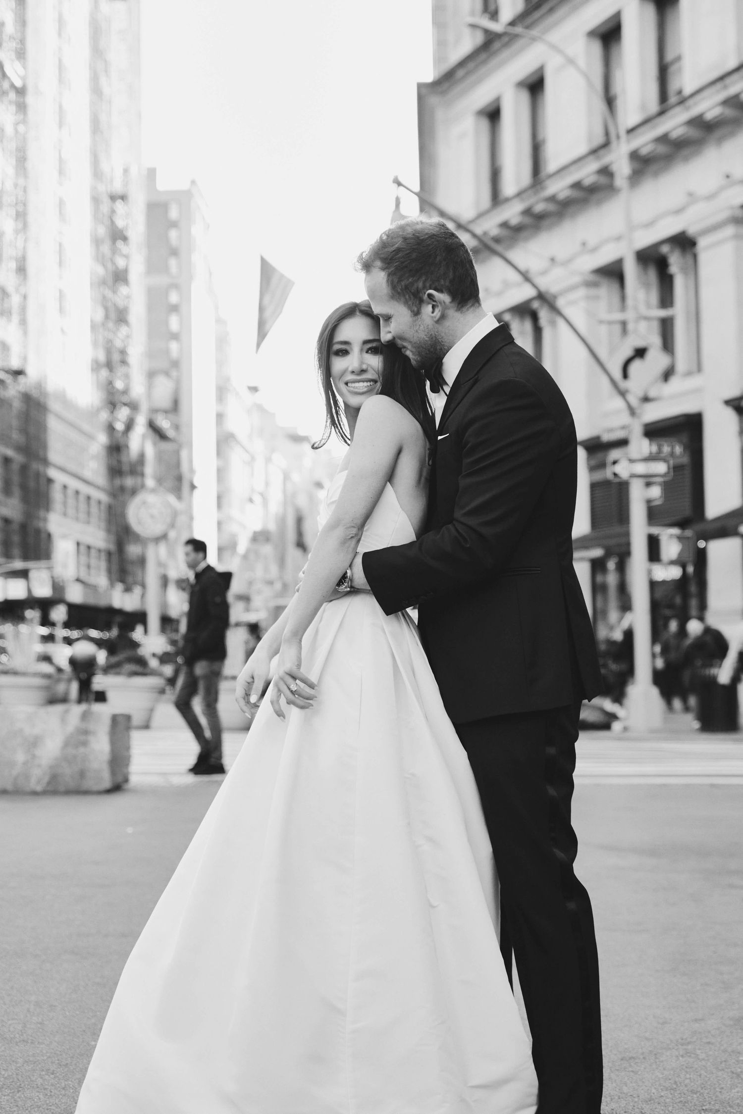 A romantic black and white wedding photo captured on a city street with elegant bridal gown and classic tuxedo.