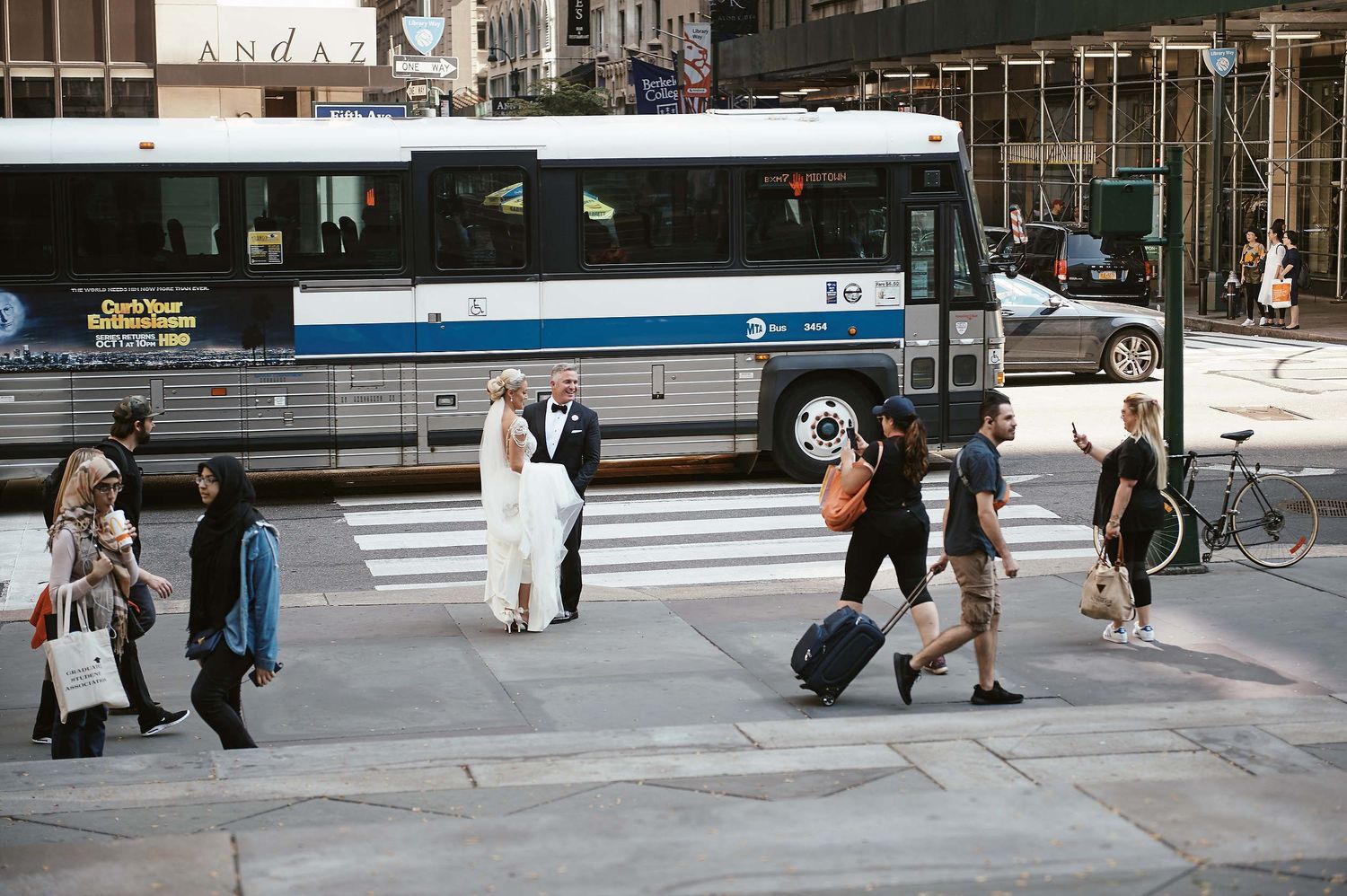 People crossing a busy city street with a New York City bus in the background.