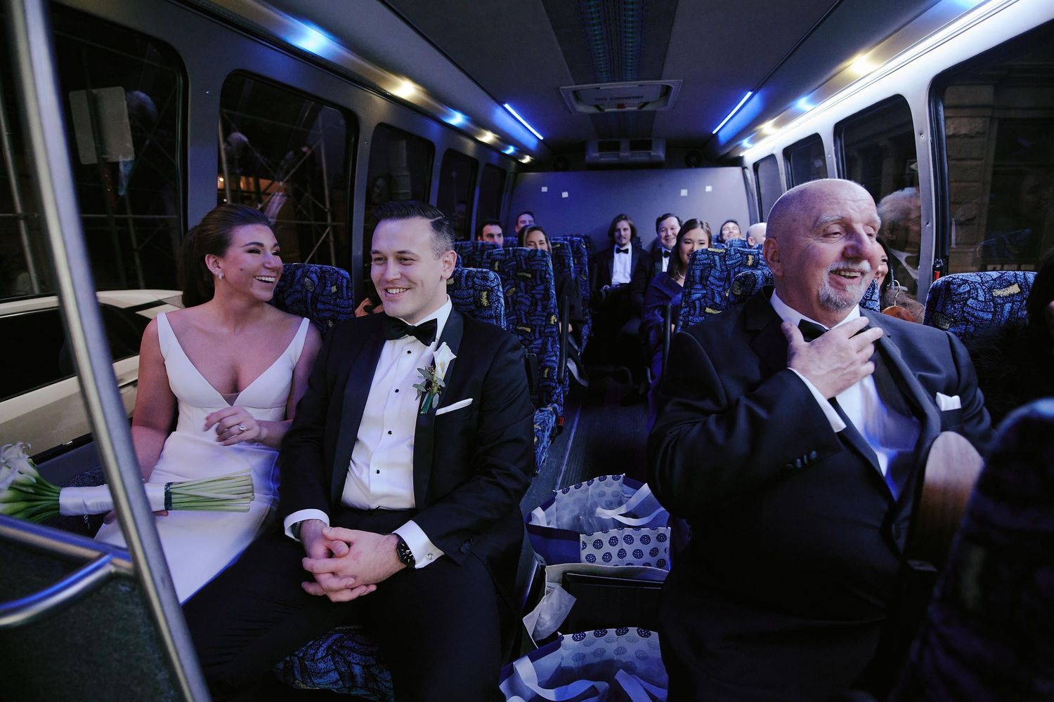 Wedding party members riding together in a limo bus with blue interior lighting.