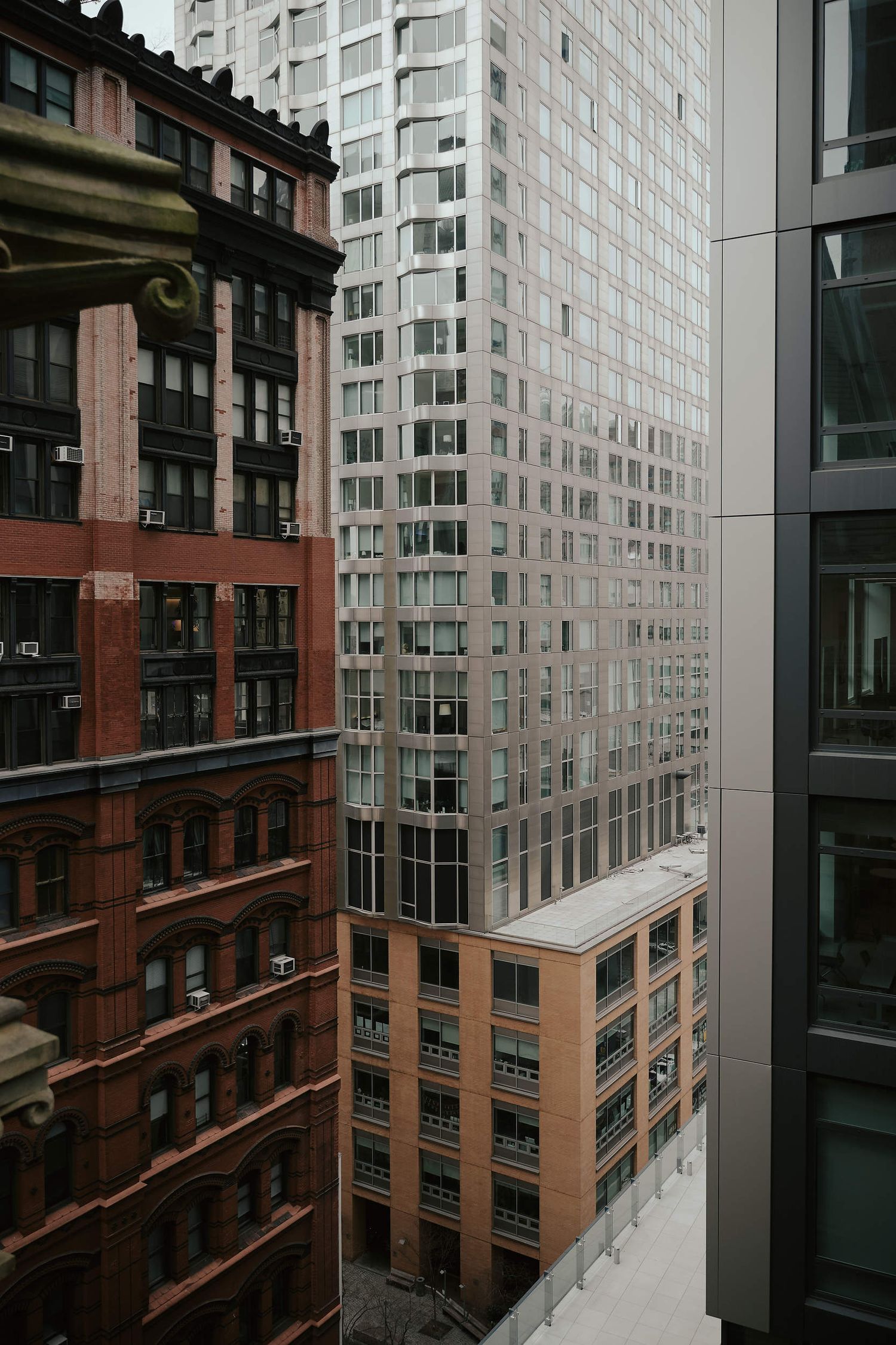 Urban architectural contrast between historic red brick buildings and modern glass skyscrapers in a dense city setting.
