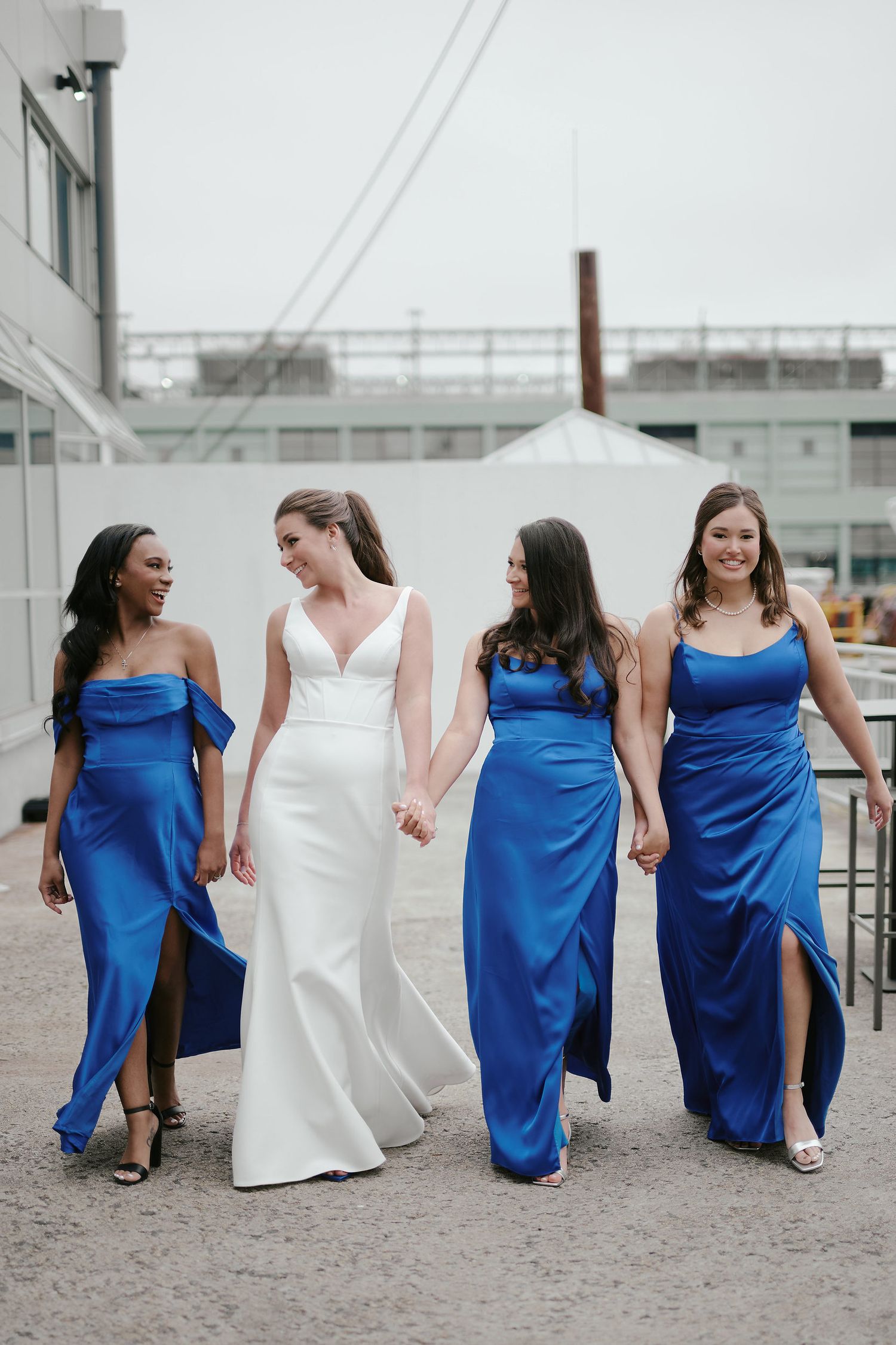 Wedding party in coordinated white and royal blue dresses walking together outdoors in an urban setting.
