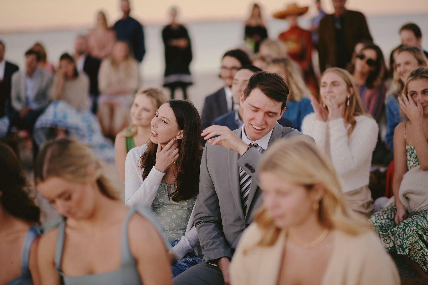 Guests enjoying and reacting to moments during an outdoor beach wedding ceremony.
