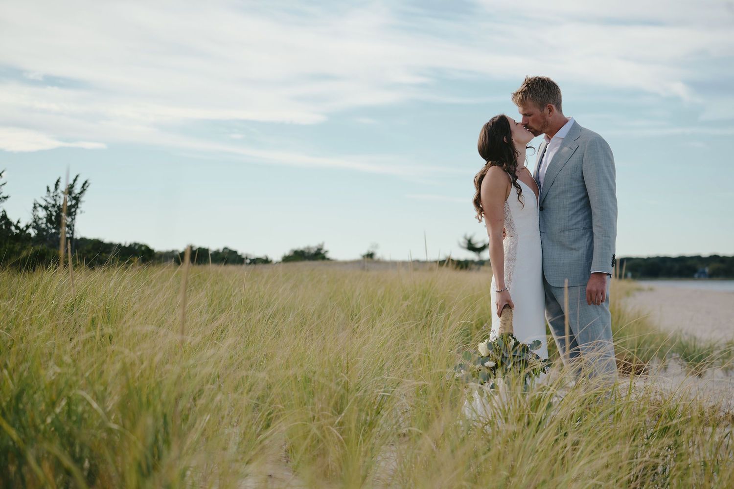 A couple shares an intimate moment in a tall grass field by the water on their wedding day.