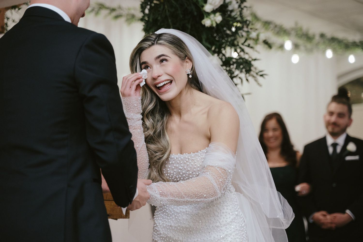A candid moment during an indoor wedding ceremony shows a couple exchanging vows under a decorated tent canopy.