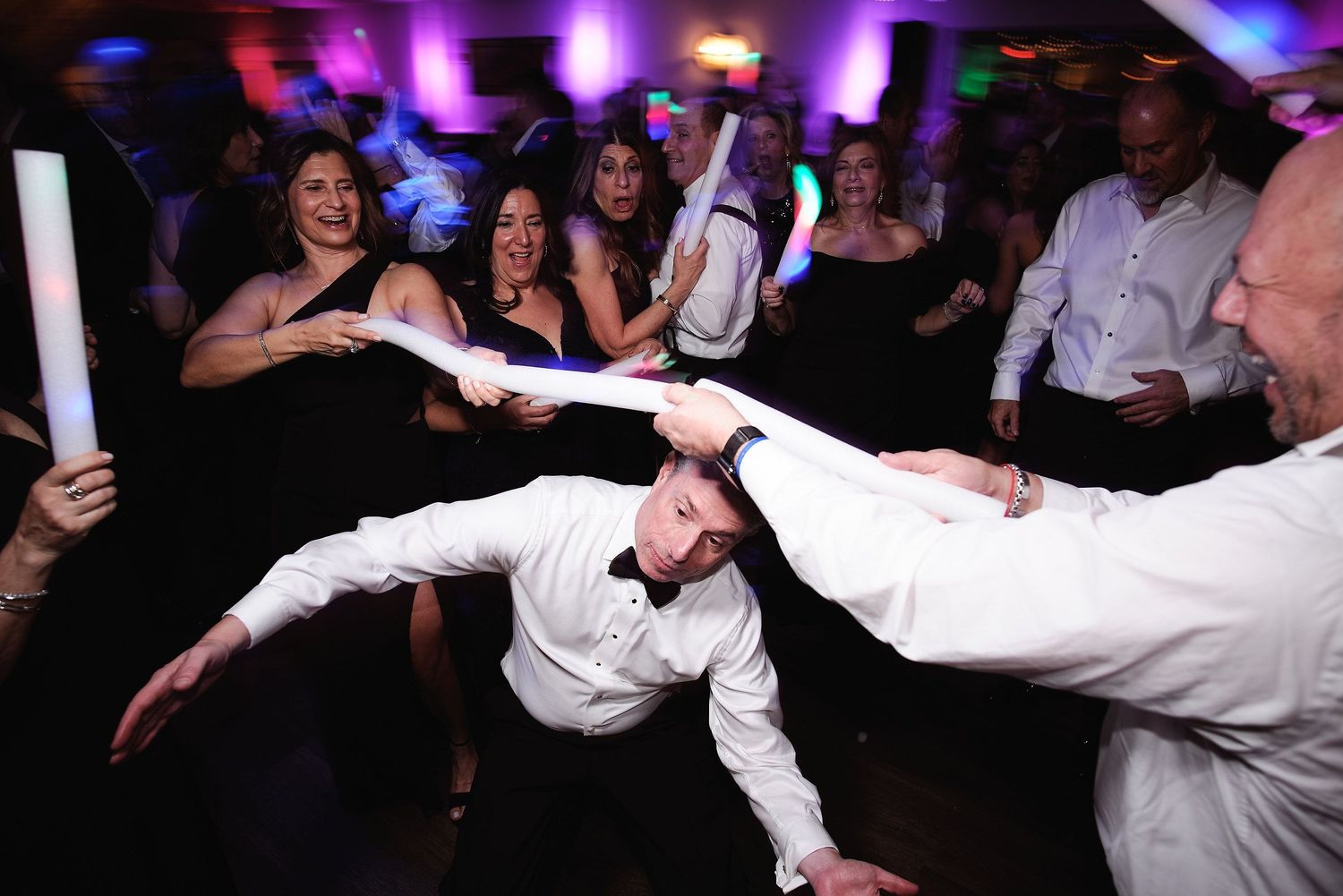 Dancers show off impressive limbo moves on a crowded dance floor with colorful purple lighting in the background.