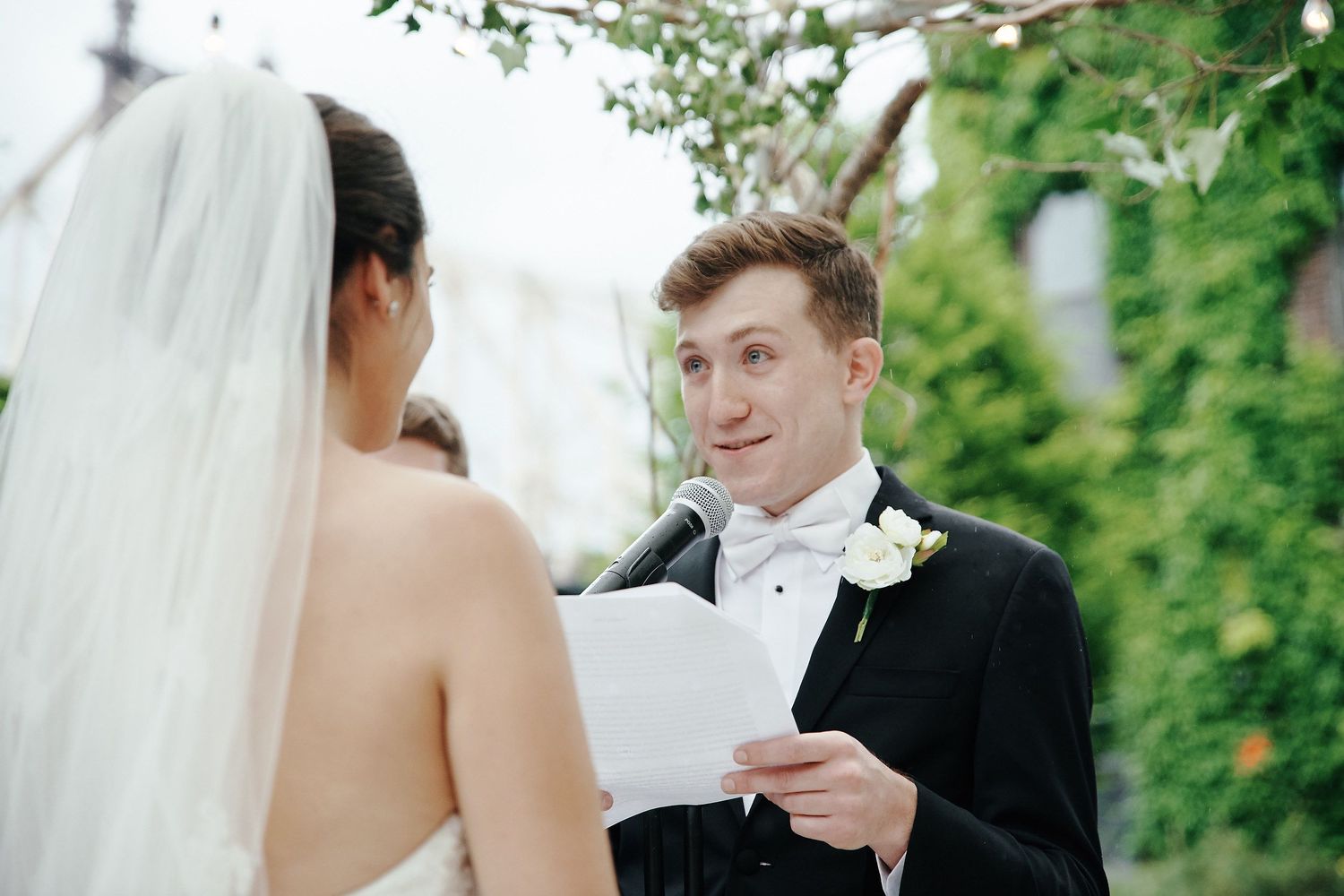 A couple exchanges personal vows during their outdoor wedding ceremony with greenery in the background.