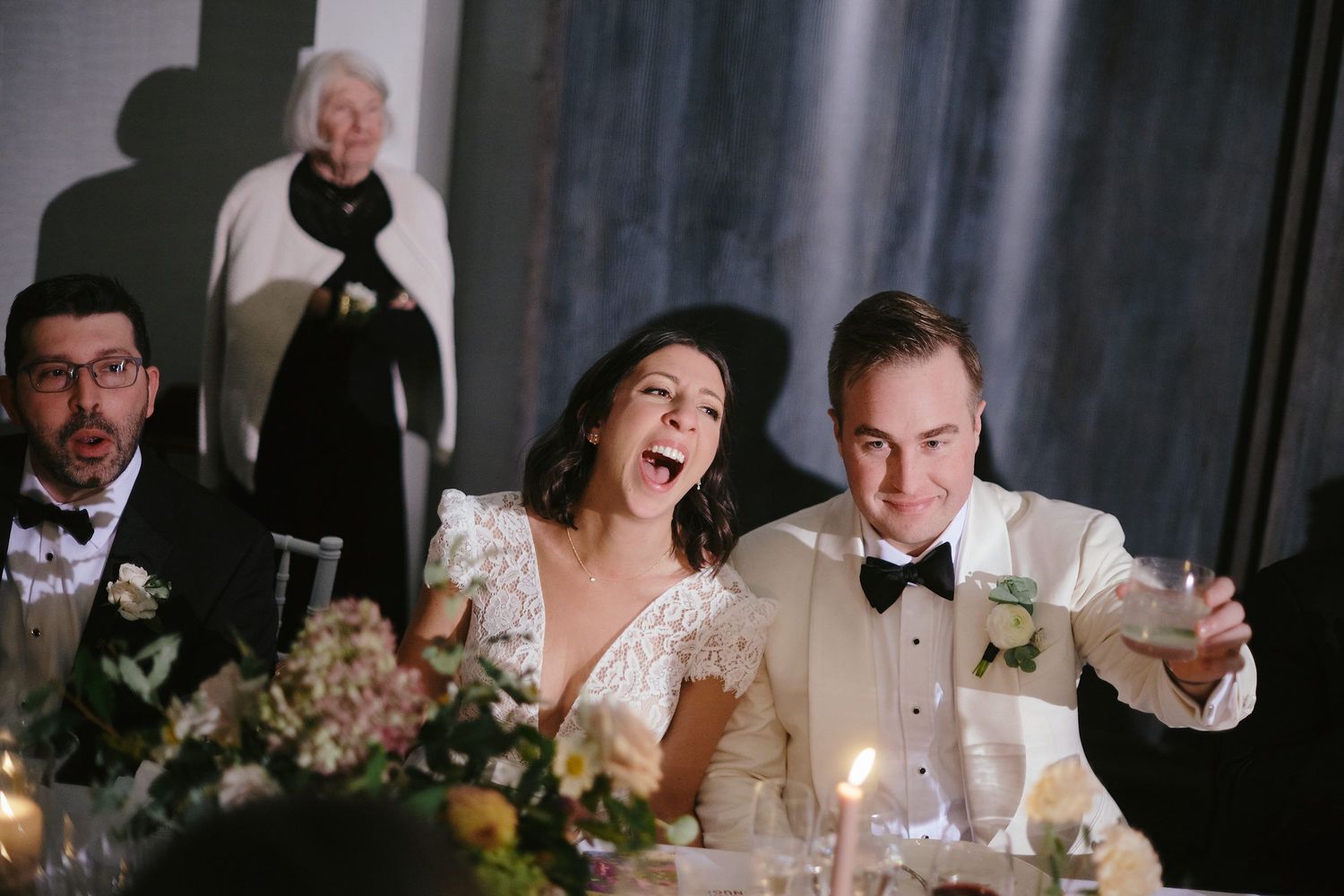 Wedding guests share a candid moment of laughter during a reception dinner at an elegant venue.