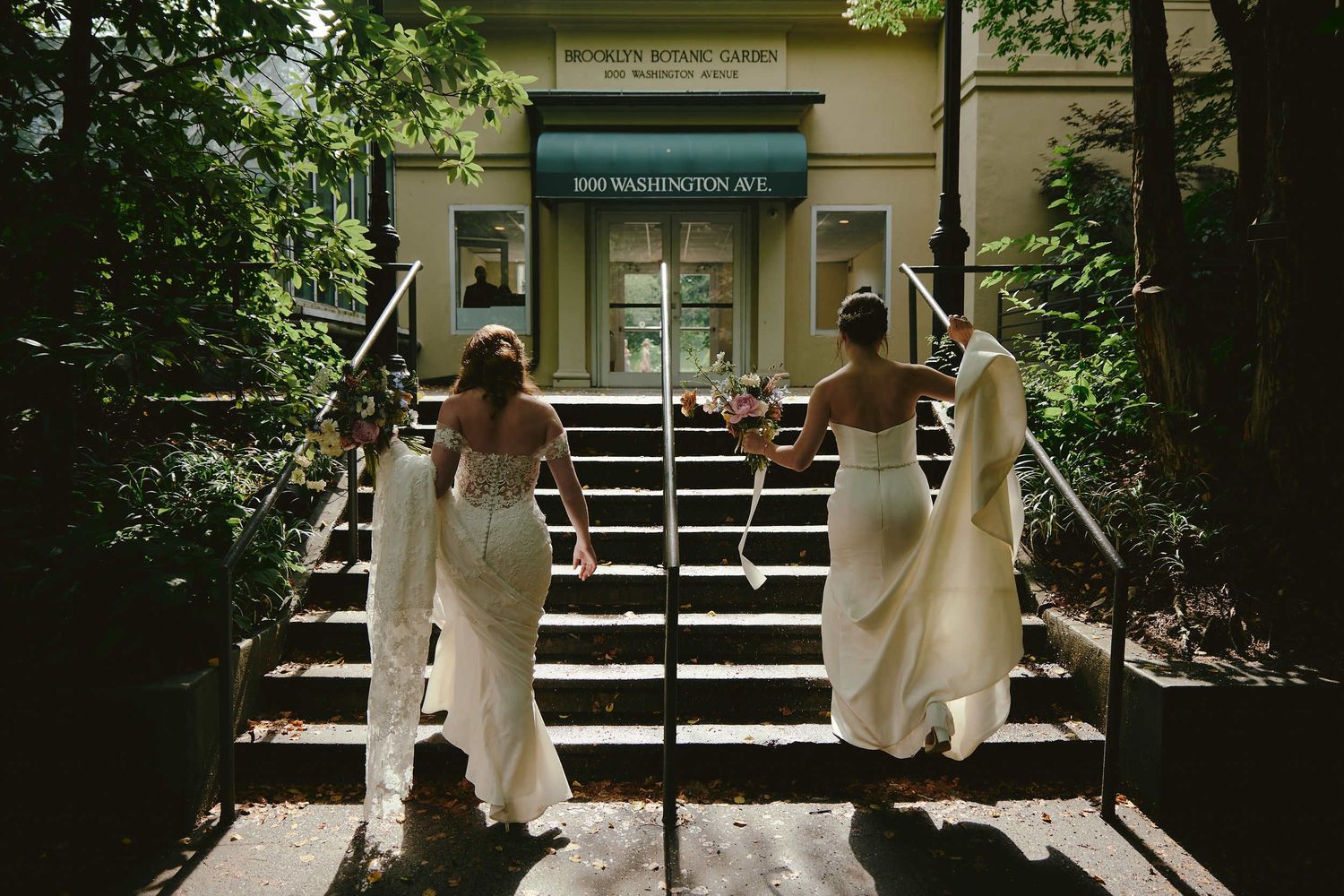Three figures in flowing white dresses walk down steps outside a building entrance in a candid outdoor scene.