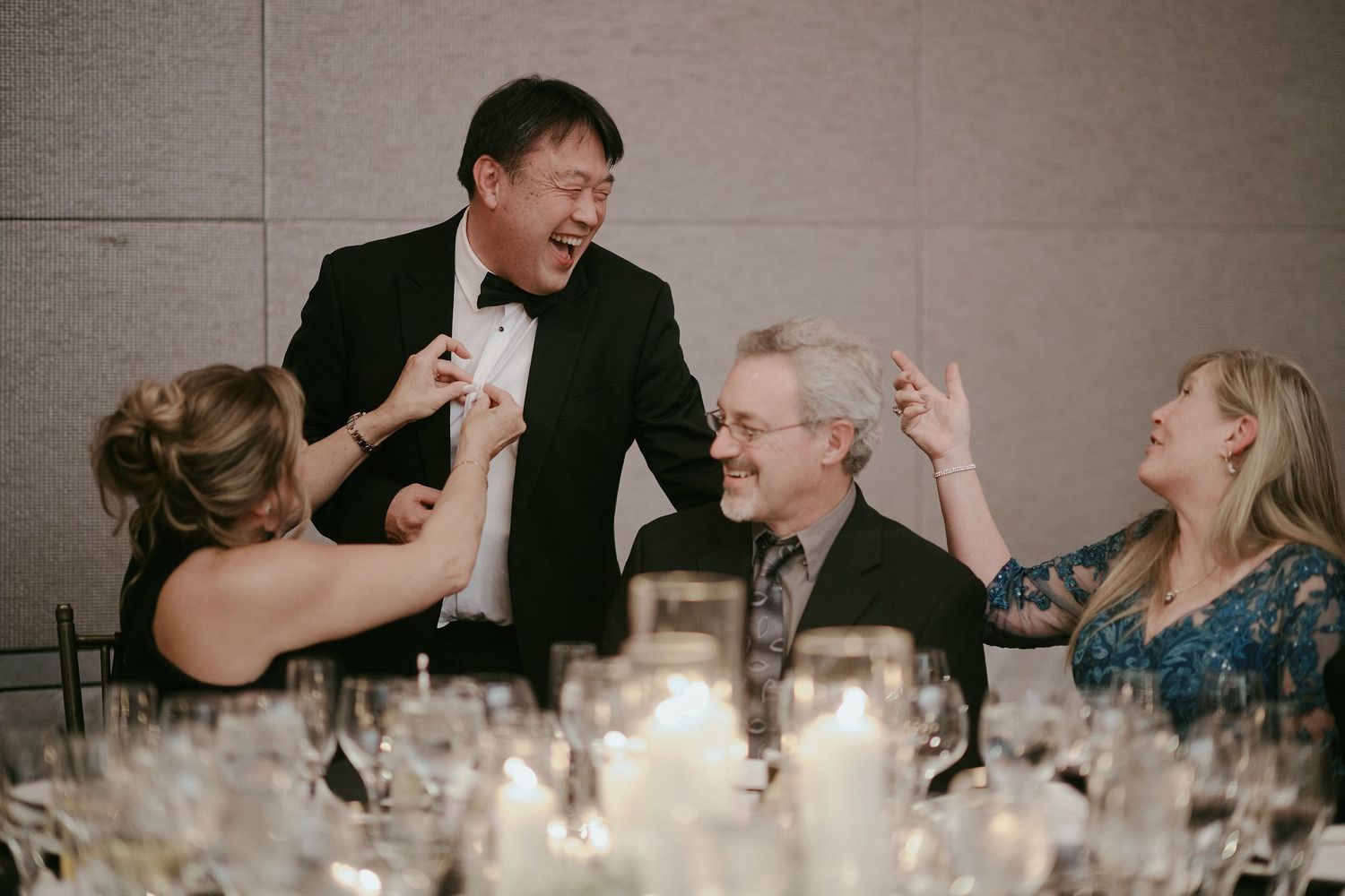 Guests share a candid moment of laughter during a formal dinner reception with candlelit tables.