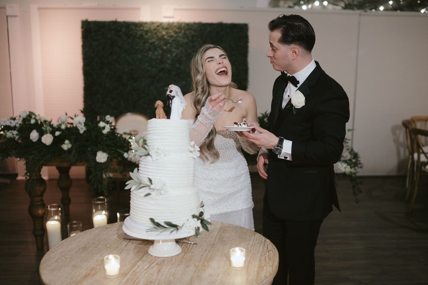 A joyful couple sharing a moment while cutting their elegant white wedding cake surrounded by candlelight.