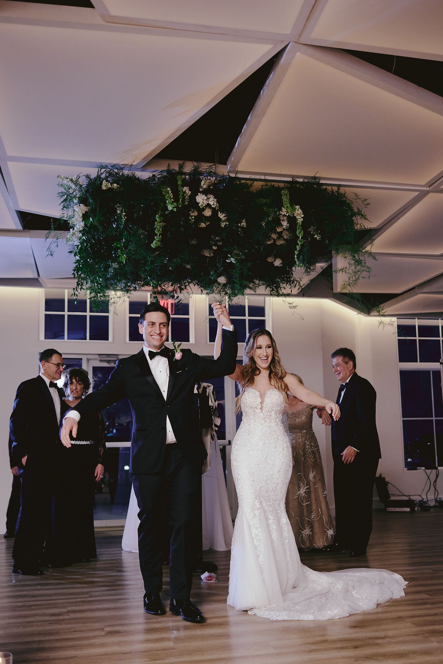 A couple celebrates during their first dance in an elegant indoor wedding venue with greenery hanging from the ceiling.