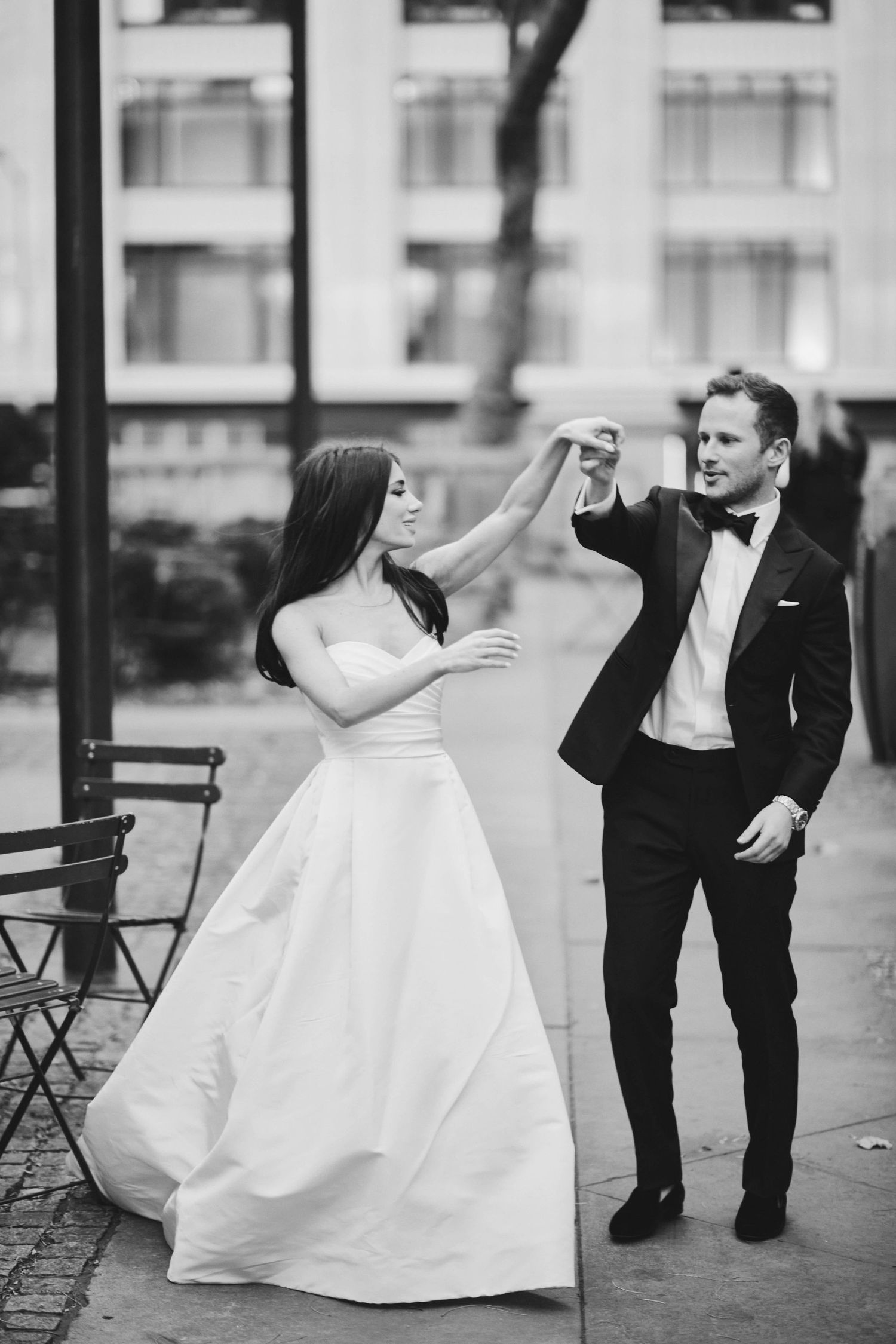 A bride in a white ballgown and groom in tuxedo playfully dance together in black and white photography.