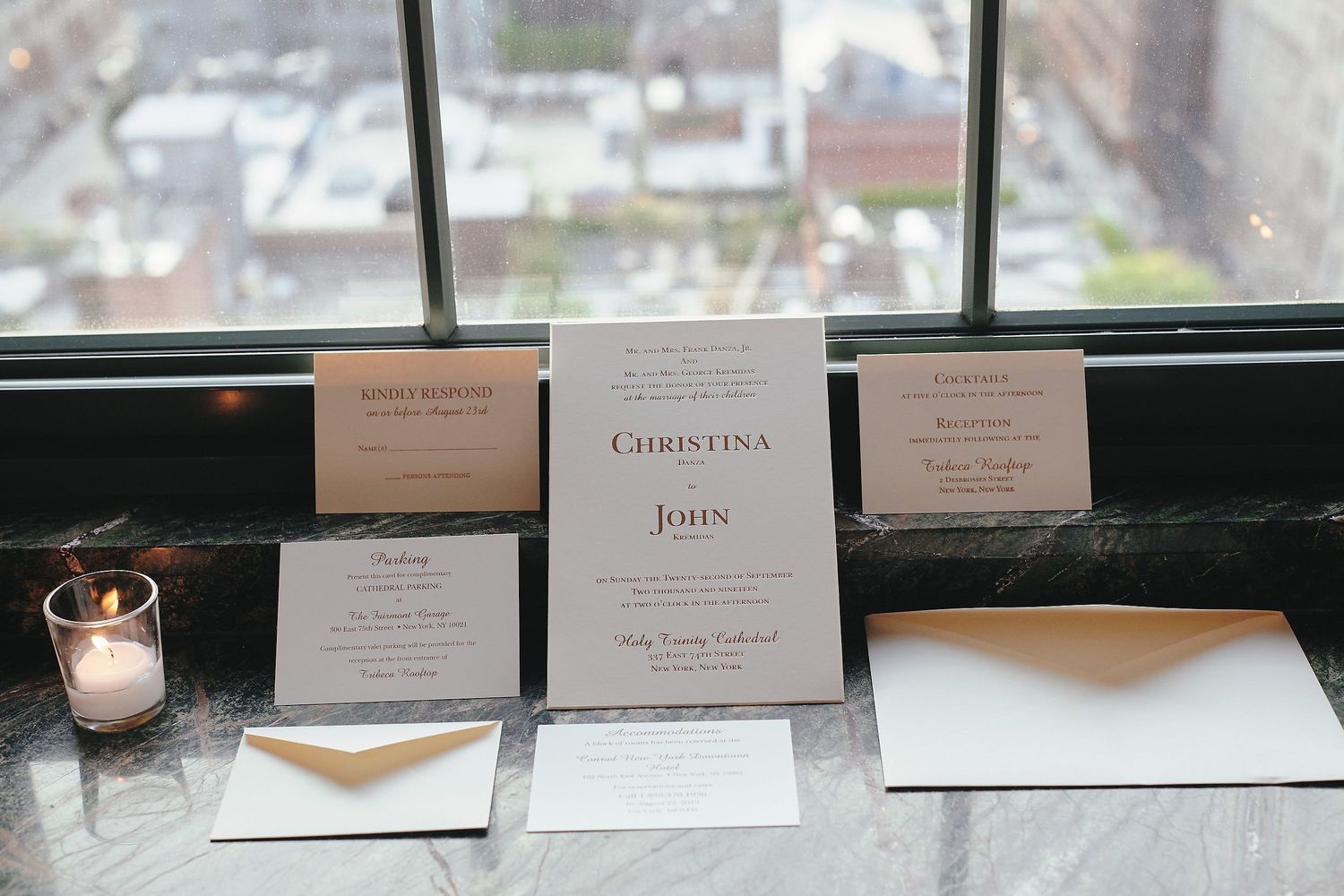Elegant wedding invitations and stationery displayed on a windowsill with a candle and city view.