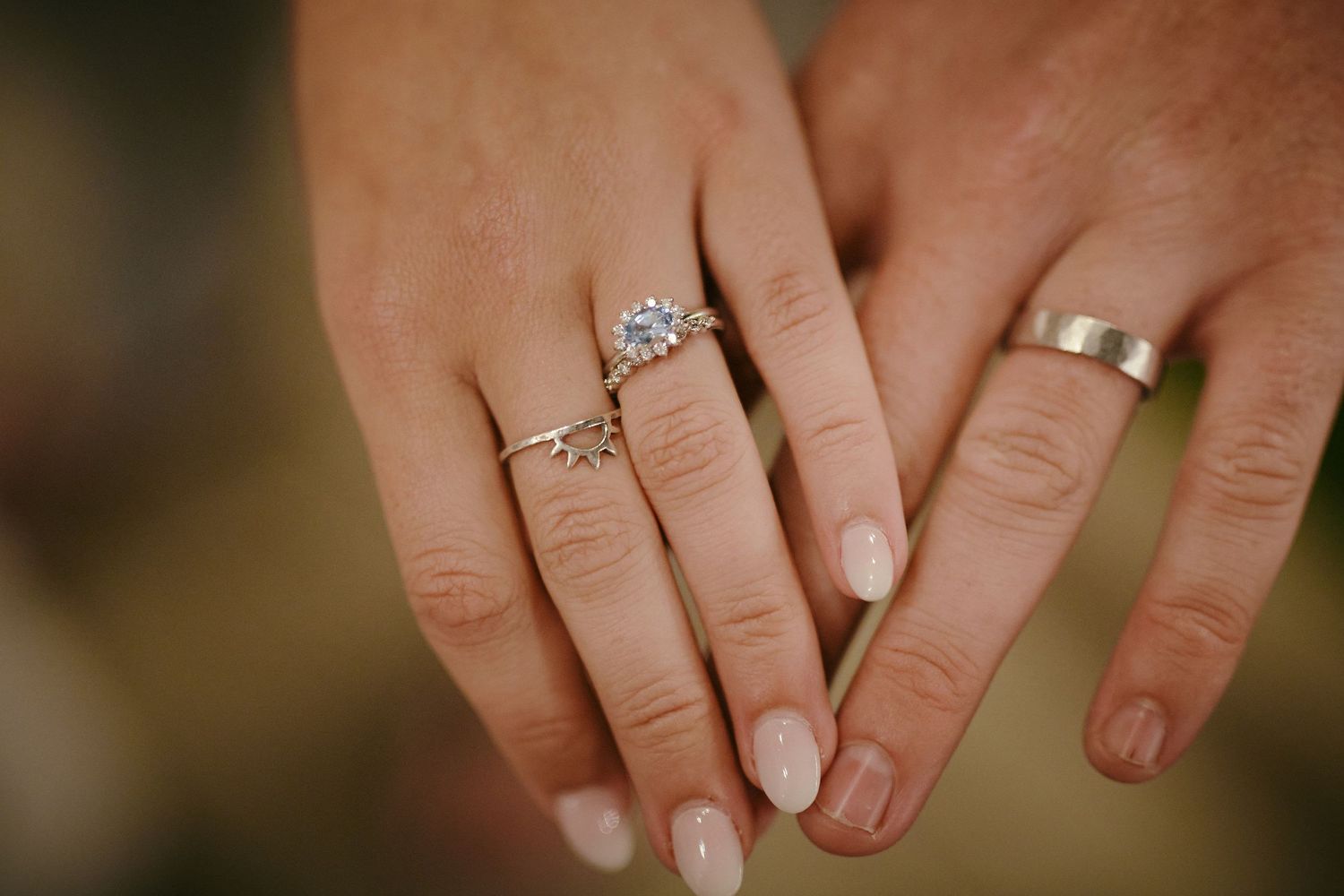 Two hands with wedding rings showing a close up of engagement and wedding bands with sparkly diamond details and neutral manicures.