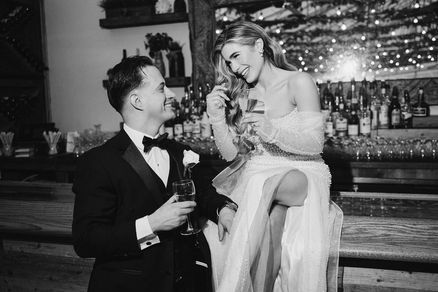 A couple in formal attire shares a romantic moment at a bar, with the bride sitting elegantly on the counter.