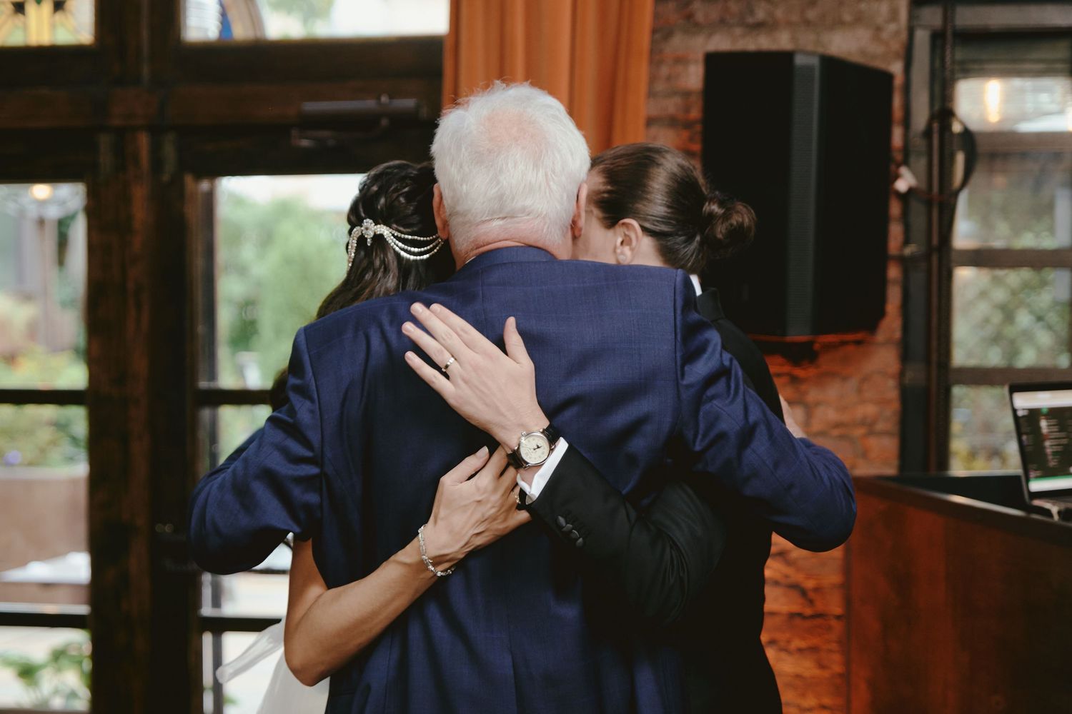 Two people share an emotional slow dance embrace at an indoor venue with wooden walls and speakers.