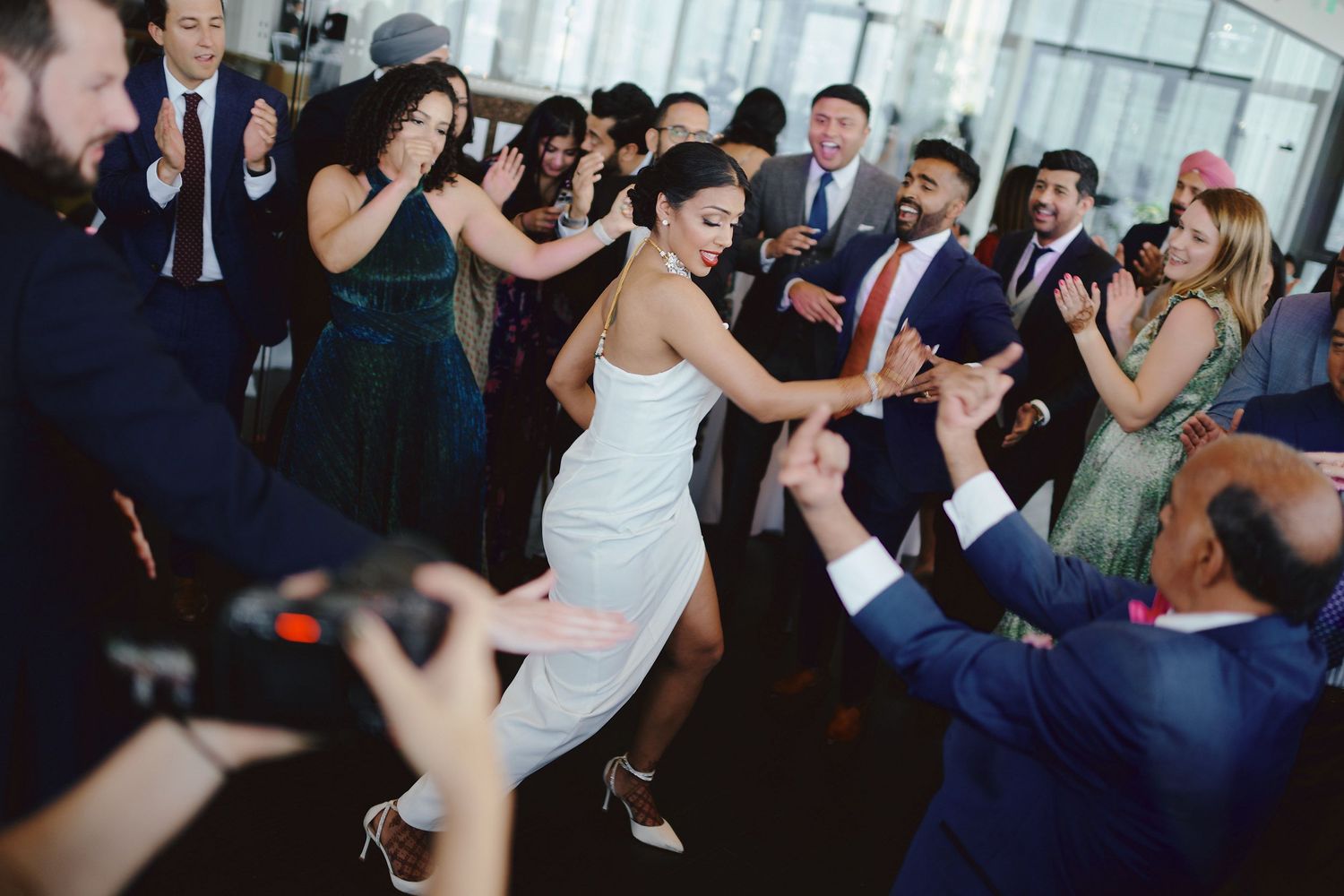 Wedding guests dance and celebrate energetically at a reception party with people in formal attire on the dance floor.