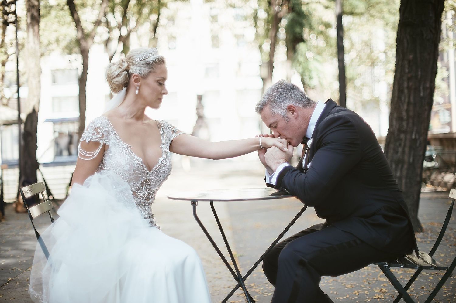 Tender wedding moment captured in an outdoor garden setting with elegant white gown and formal black suit.