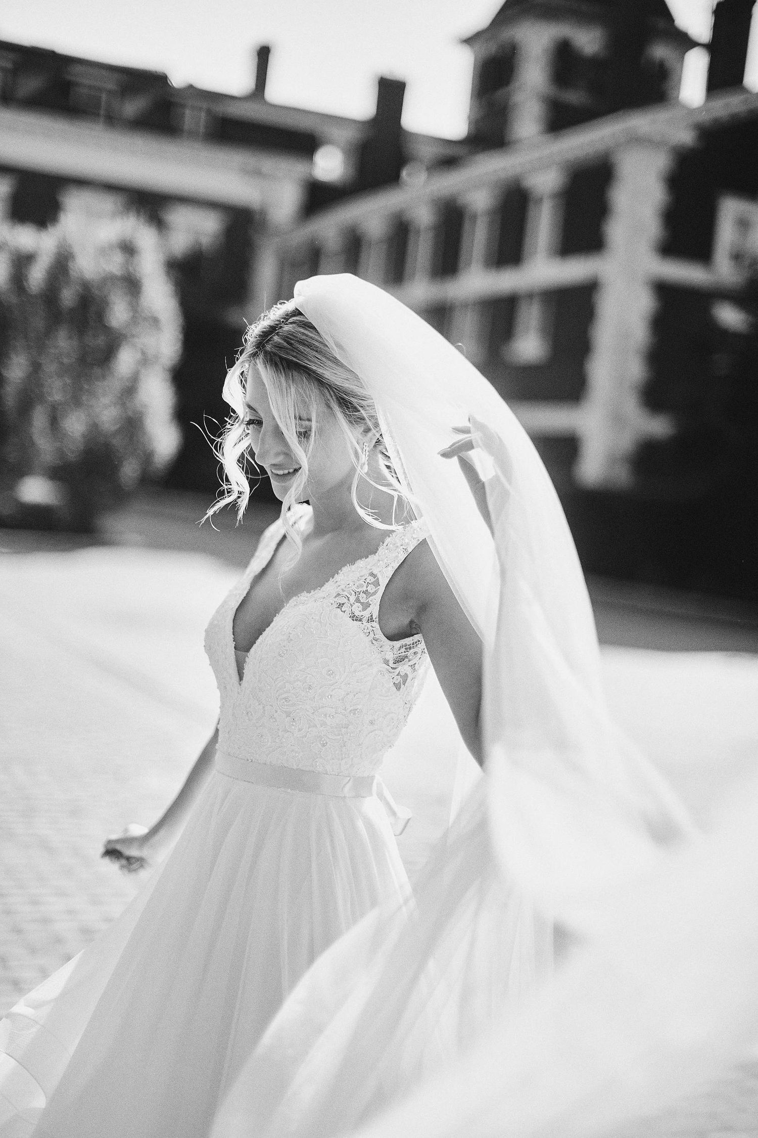 Black and white wedding photograph of a bride in a flowing lace gown and veil walking outdoors on her special day.
