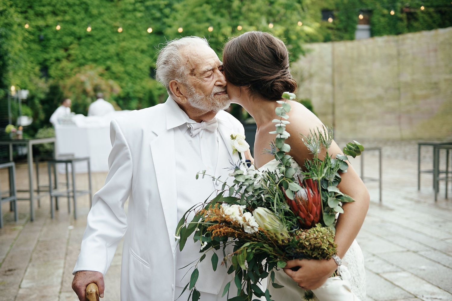A tender moment between two people at a wedding event with rustic greenery and floral bouquet.
