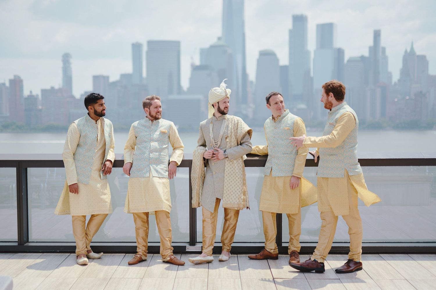 Wedding party in cream kurtas poses against NYC skyline backdrop.