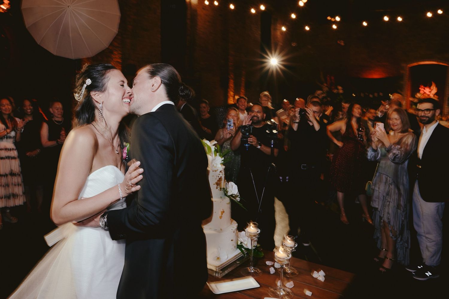A couple shares their first dance at a romantic evening wedding reception with twinkle lights and guests watching.