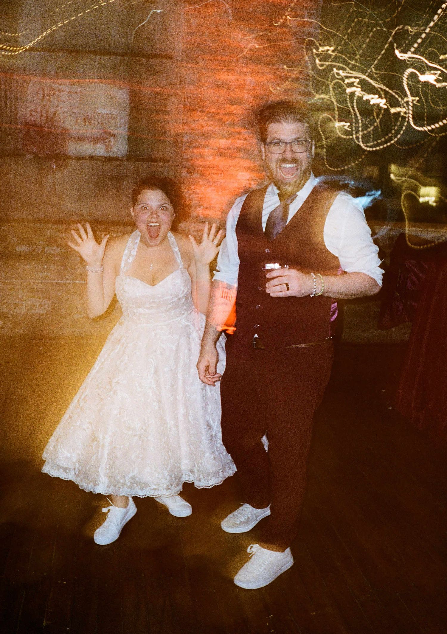 Wedding couple in vintage-style photo wearing white dress and vest dancing together on their celebration evening.