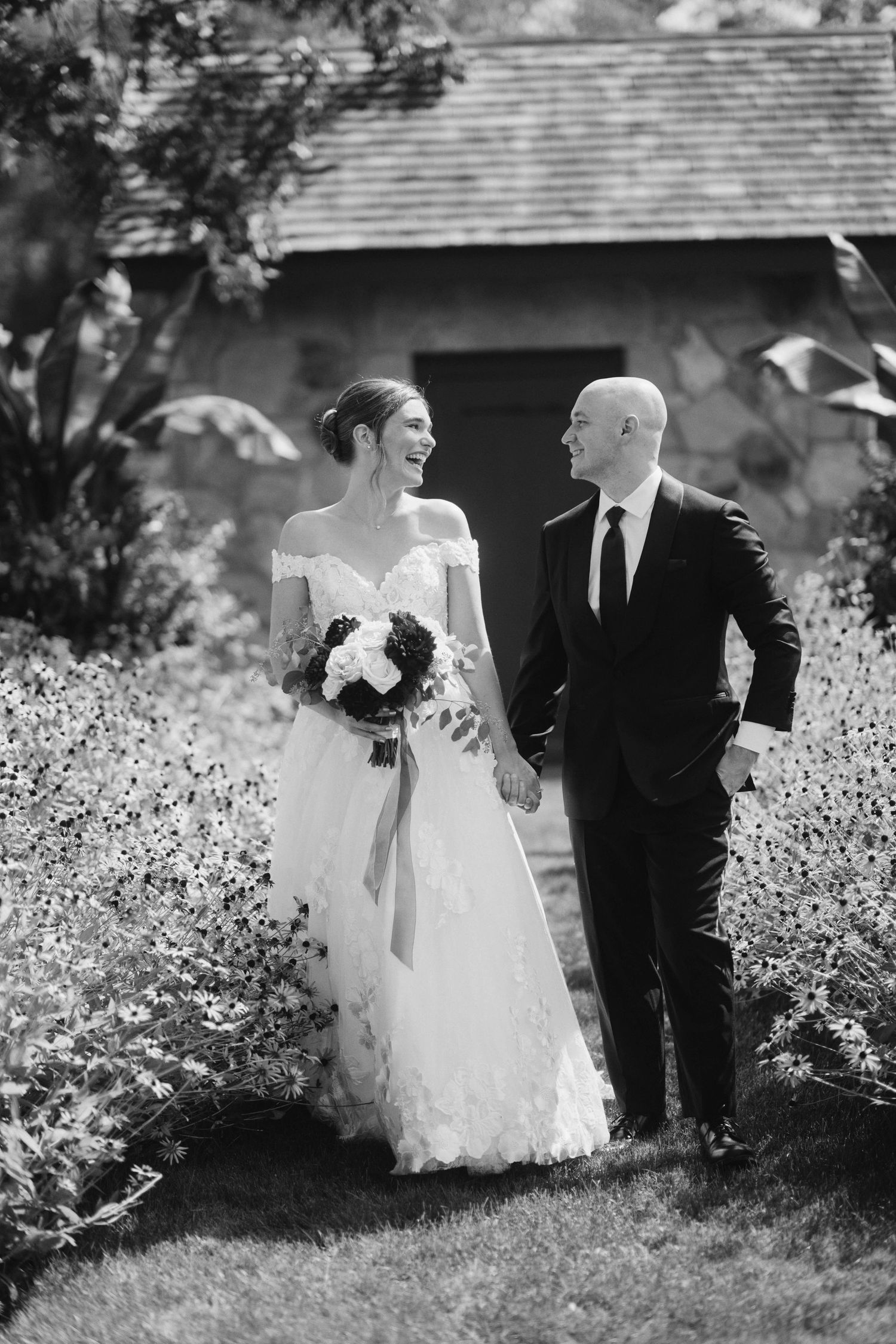 Black and white wedding photos showing a couple walking through a garden with white flowers in a romantic sequence.