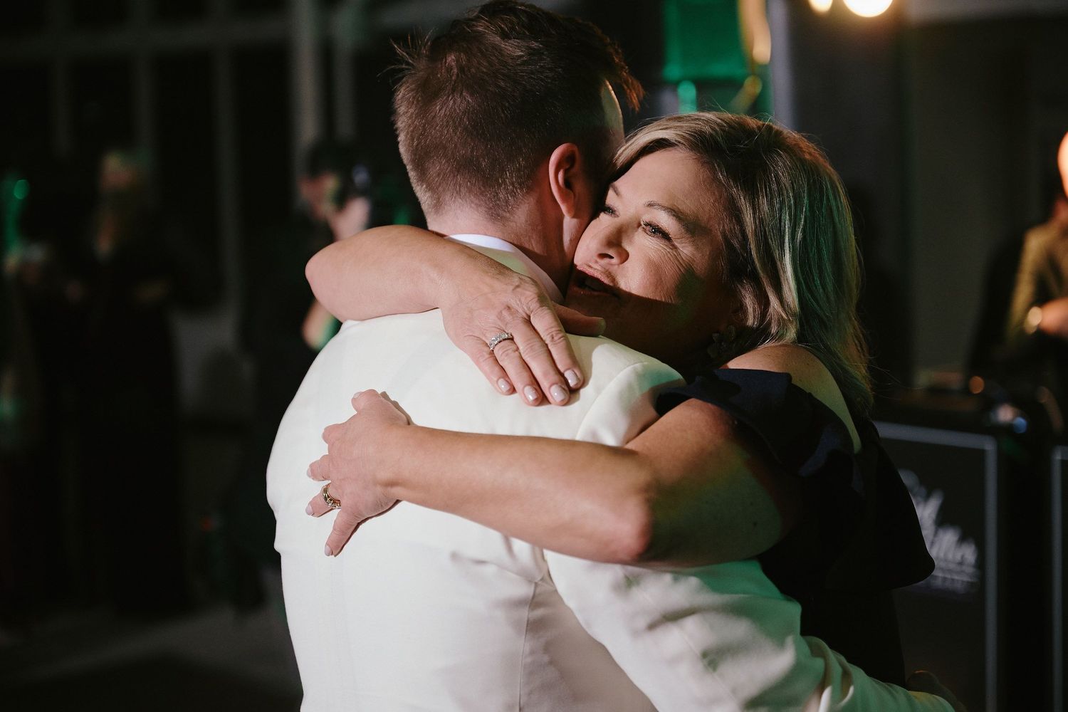A warm embrace shared between two people at a dimly lit evening event.