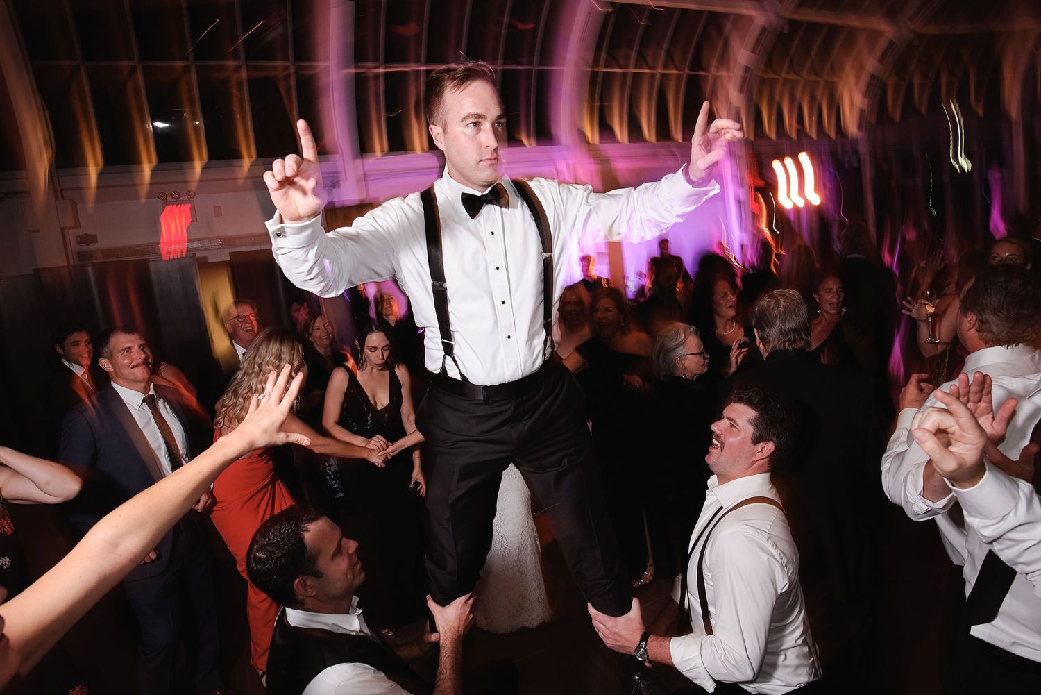 Energetic wedding reception celebration with someone being lifted up by the crowd on a lively dance floor.