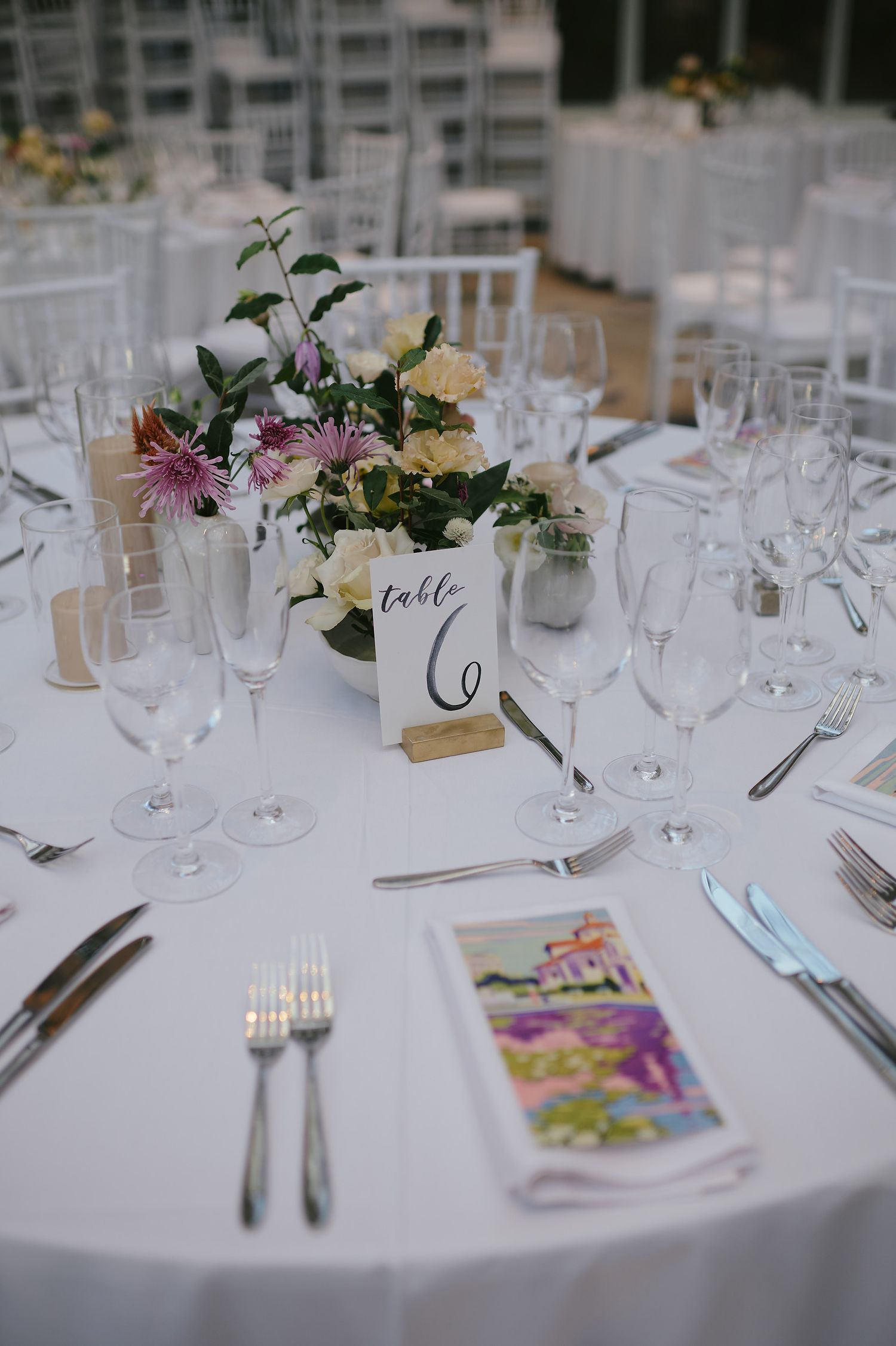 Elegant table setting at a wedding reception with white linens, wine glasses, cutlery and pastel floral centerpiece.