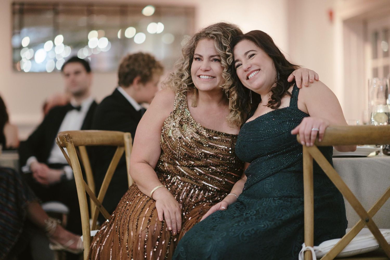 Two guests in elegant evening gowns share a joyful moment at a formal event.