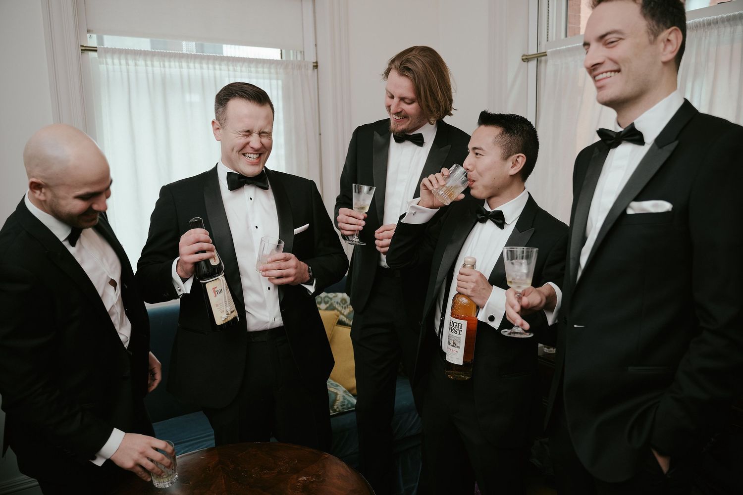 A group of men in tuxedos share drinks and laughs during a formal gathering.